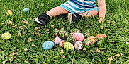 Tobias is registered to the contest to win money with this photo: child, toddler, boy, striped_clothing, blue_stripes, grass, easter_eggs, camouflage_egg, clover, sitting, outdoor, portrait, blond_hair, black_shoes, toy, truck_wheel, vehicle, lawn, curious_expression, greenery