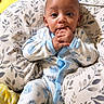 baby, infant, child, portrait, indoors, bed, pillow, blanket, pajamas, blue_clothing, yellow_blanket, sitting, lying_down, wide_eyed, hand_to_mouth, smiling, cozy, bedding, floral_pattern, home