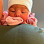 baby, newborn, infant, hat, pink_clothing, sleepy, close_up, person, shoulder, hand, face, skin, cozy, indoor, soft_light, cute, tender, resting, warm, newborn_hat