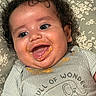 baby, child, curly_hair, smiling, happy, food_mess, face, clothing, shirt, elephant_graphic, text_on_clothing, blanket, floral_pattern, lying_down, infant, cute, joyful, portrait, close_up, messy