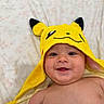 baby, child, smiling, face, hooded_towel, pikachu, yellow, cute, happy, lying_down, blanket, skin, cheeks, eyes, mouth, infant, indoors, portrait, towel, expression