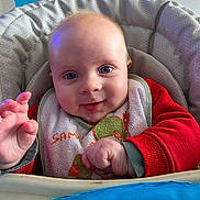 Basile a rejoint le concours — aidez-le/la à gagner de superbes lots ! baby, child, high_chair, bib, red_clothing, smiling, blue_eyes, hand, face, indoor, cushion, person, infant, happy, cute, young, portrait, table, feeding, bright