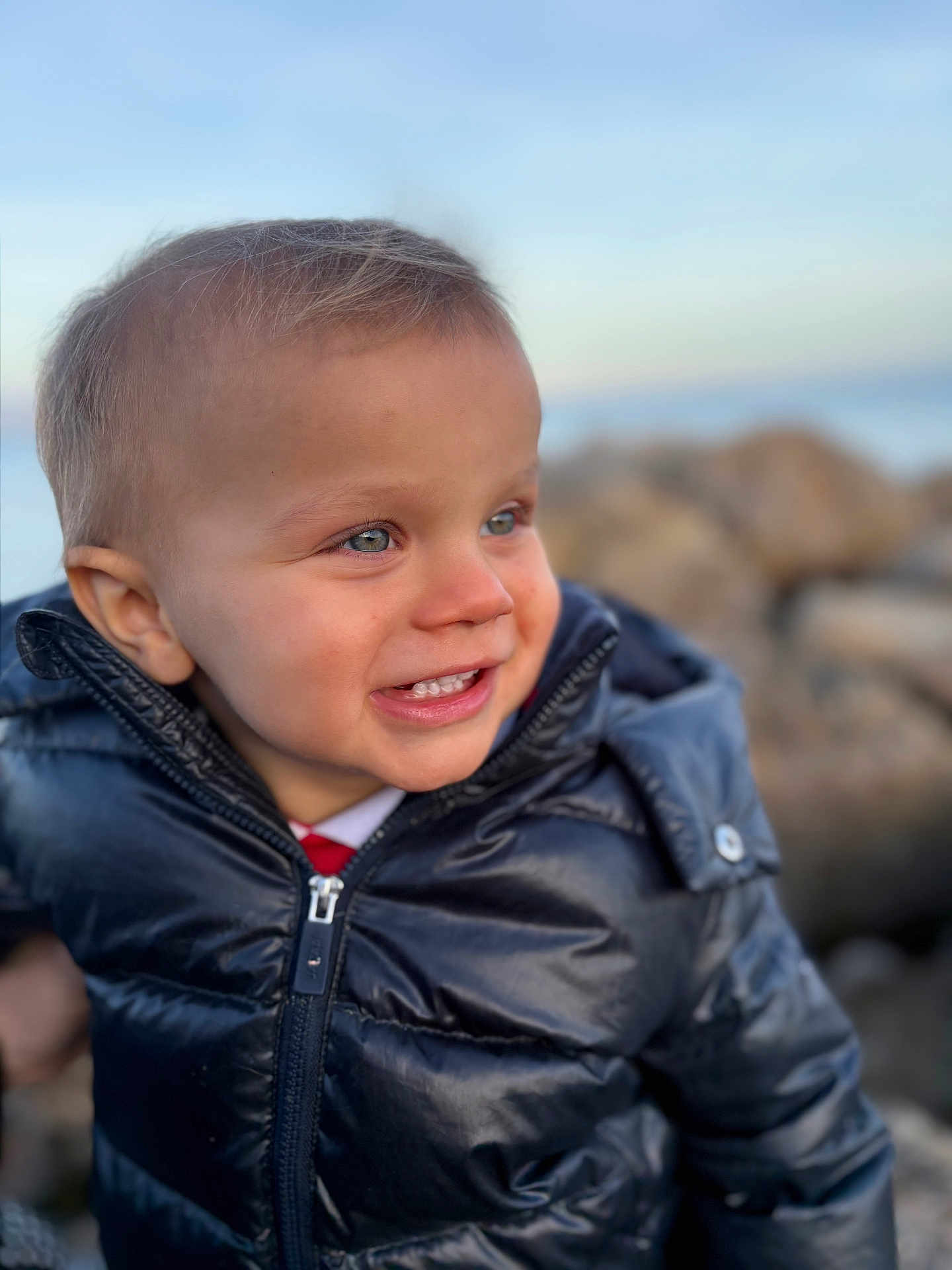 Levi participe au concours pour gagner de l'argent avec cette photo : child, toddler, smile, jacket, black_jacket, outdoor, portrait, happy, face, blue_eyes, short_hair, nature, rocks, sky, young_child, winter_clothing, closeup, cute, person, daylight