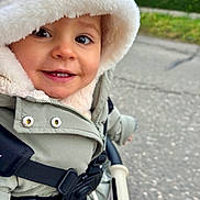 Gina participe au concours pour gagner de l'argent avec cette photo : toddler, child, smiling, hood, jacket, stroller, outdoor, cold_weather, baby, happy, face, clothing, zipper, safety_strap, hand, nature, greenery, pavement, cute, portrait
