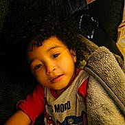 Isaiah joined the competition — help win amazing prizes! child, curly_hair, blanket, toddler, indoor, couch, red_shirt, cartoon_characters, relaxing, portrait, soft_lighting, face, comfort, warm, young_child, smiling, cozy, person, closeup, casual