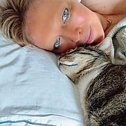Marius participe au concours pour gagner de l'argent avec cette photo : person, cat, tabby_cat, face, blue_eyes, pillow, bed, blanket, snuggling, closeup, resting, fur, whiskers, nose, skin, hair, necklace, indoor, cozy, relaxed
