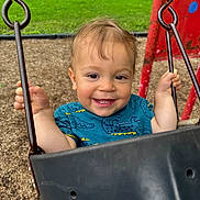 Aiden joined the competition — help win amazing prizes! child, toddler, swing, playground, smiling, happy, outdoor, grass, woodchips, metal, chain, blue_shirt, person, baby, fun, summer, park, face, cute, joy