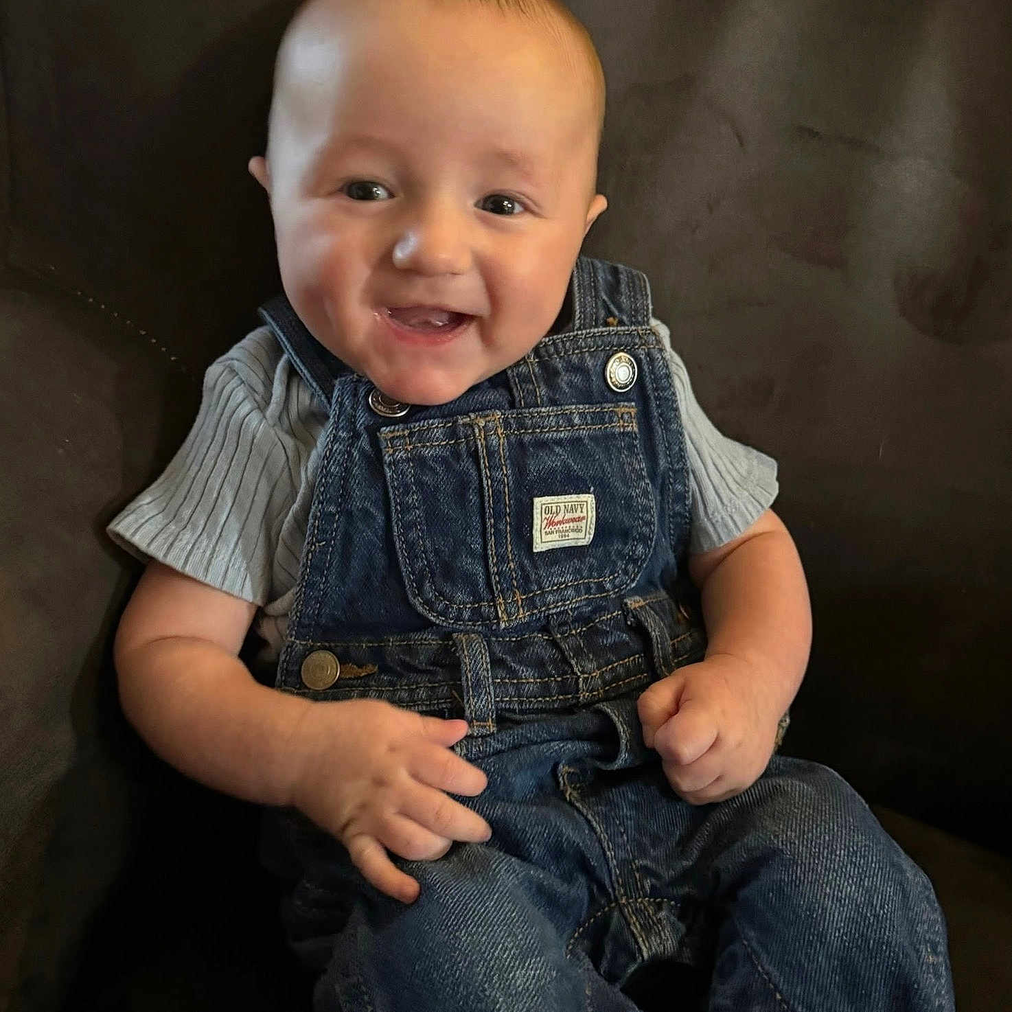 Warren joined the competition — help win amazing prizes! baby, casual, child, clothing, couch, cute, denim_overalls, face, grey_shirt, hands, happy, head, indoor, infant, person, portrait, sitting, skin, smiling, young