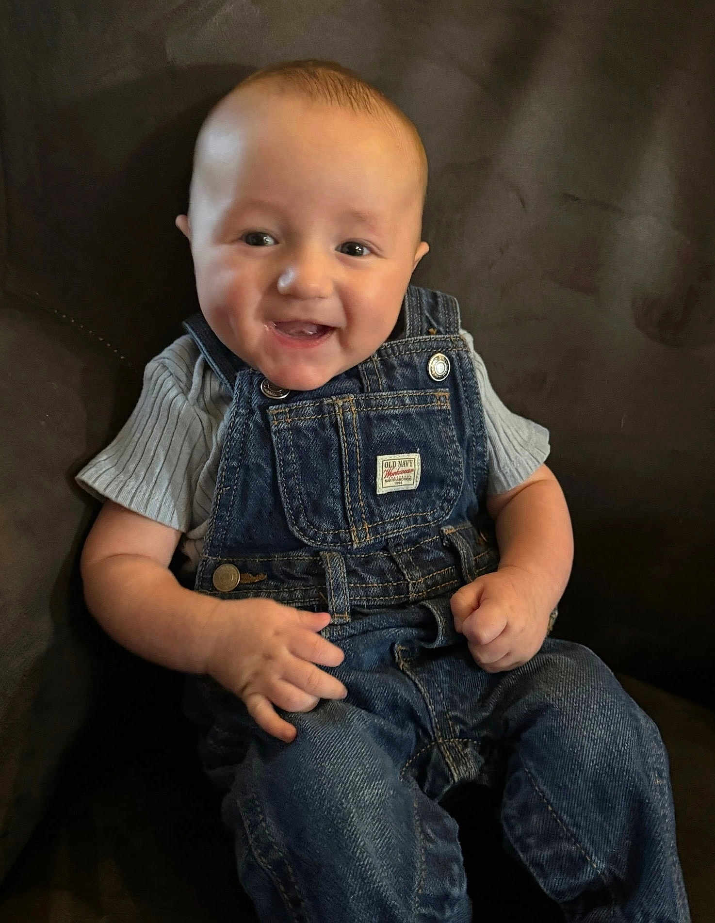 Warren joined the competition — help win amazing prizes! baby, child, smiling, denim_overalls, grey_shirt, couch, happy, infant, portrait, sitting, person, clothing, indoor, cute, young, face, skin, hands, head, casual