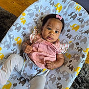Fimidara is registered to the contest to win money with this photo: baby, infant, child, pink_bow, pink_clothing, white_tights, elephant_pattern, cushion, baby_seat, floor, wooden_floor, carpet, indoor, portrait, cute, looking_at_camera, small_hands, curious_expression, infant_fashion, comfort