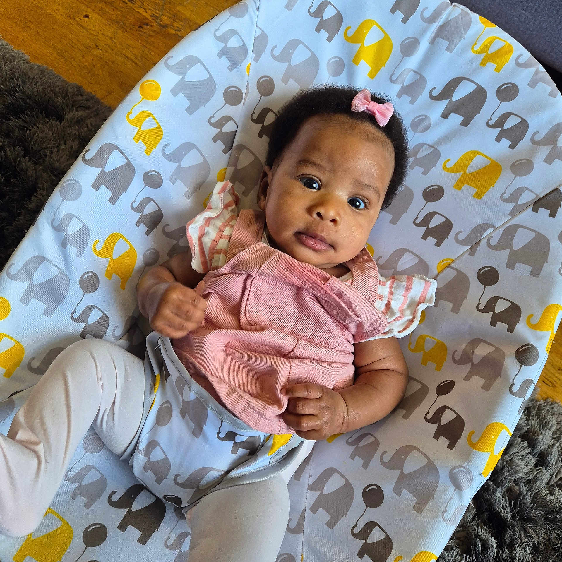 Fimidara is registered to the contest to win money with this photo: baby, infant, child, pink_bow, pink_clothing, white_tights, elephant_pattern, cushion, baby_seat, floor, wooden_floor, carpet, indoor, portrait, cute, looking_at_camera, small_hands, curious_expression, infant_fashion, comfort