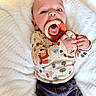 Jasper joined the competition — help win amazing prizes! baby, infant, teething_ring, wooden_toy, crocheted_toy, blanket, clothing, patterned_shirt, pants, face, hands, mouth, eyes, lying_down, cute, soft_texture, indoor, child, person, adorable