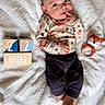 baby, infant, child, blanket, wooden_blocks, toy, knitted_toy, fox_pattern, clothing, cute, lying_down, indoor, playful, hand_on_face, expression, soft_texture, warm, portrait, young, smiling