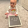baby, child, infant, carpet, letter_board, pink_tutu, white_shirt, rainbow, bear_graphic, indoor, person, cute, holding, sitting, curious, soft_lighting, floor, room, toy, letters