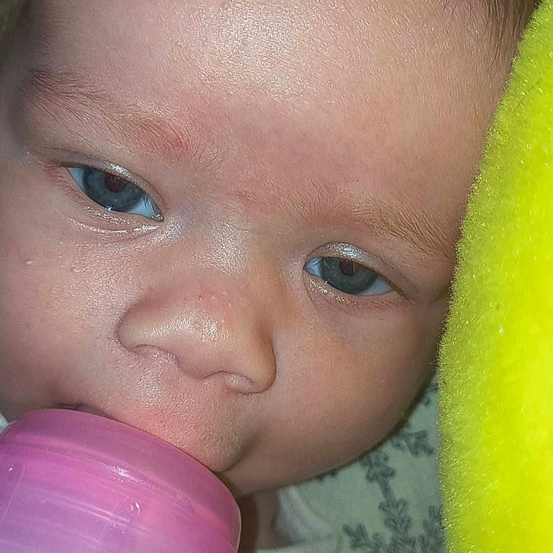 Kaleia joined the competition — help win amazing prizes! baby, blue_eyes, bottle, close_up, drinking, face, fuzzy_blanket, infant, laying_down, mouth, nose, pink_bottle, plush, skin, sleepy, soft_texture, toddler, white_clothing, yellow_blanket, young_child