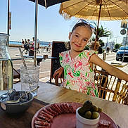 Abygail participe au concours pour gagner de l'argent avec cette photo : child, girl, smiling, outdoor, cafe, table, food, plate, sausage, pickles, glass, water, umbrella, beach, bicycle, people, sunny, daytime, dress, portrait