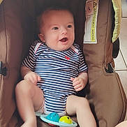 Dastan participe au concours pour gagner de l'argent avec cette photo : baby, infant, striped_onesie, brown_baby_seat, toy, happy, smiling, child, indoor, cushion, person, legs, feet, hand, head, face, seat, playful, cute, comfortable