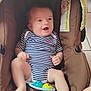 baby, infant, striped_onesie, brown_baby_seat, toy, happy, smiling, child, indoor, cushion, person, legs, feet, hand, head, face, seat, playful, cute, comfortable