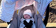 Brighton is registered to the contest to win money with this photo: newborn, baby, car_seat, infant, blanket, hat, outdoor, parking_lot, sunlight, clothing, baby_gear, safety_harness, cotton, sleeping, cute, soft_texture, gray, white, peaceful, newborn_clothing