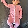 baby, baby_garment, bedspread, child, curious_expression, cute, gray_background, indoors, infant, infant_fashion, lying_down, onesie, person, pink_clothing, portrait, sleepwear, small_child, soft_fabric, striped_clothing, wide_eyes