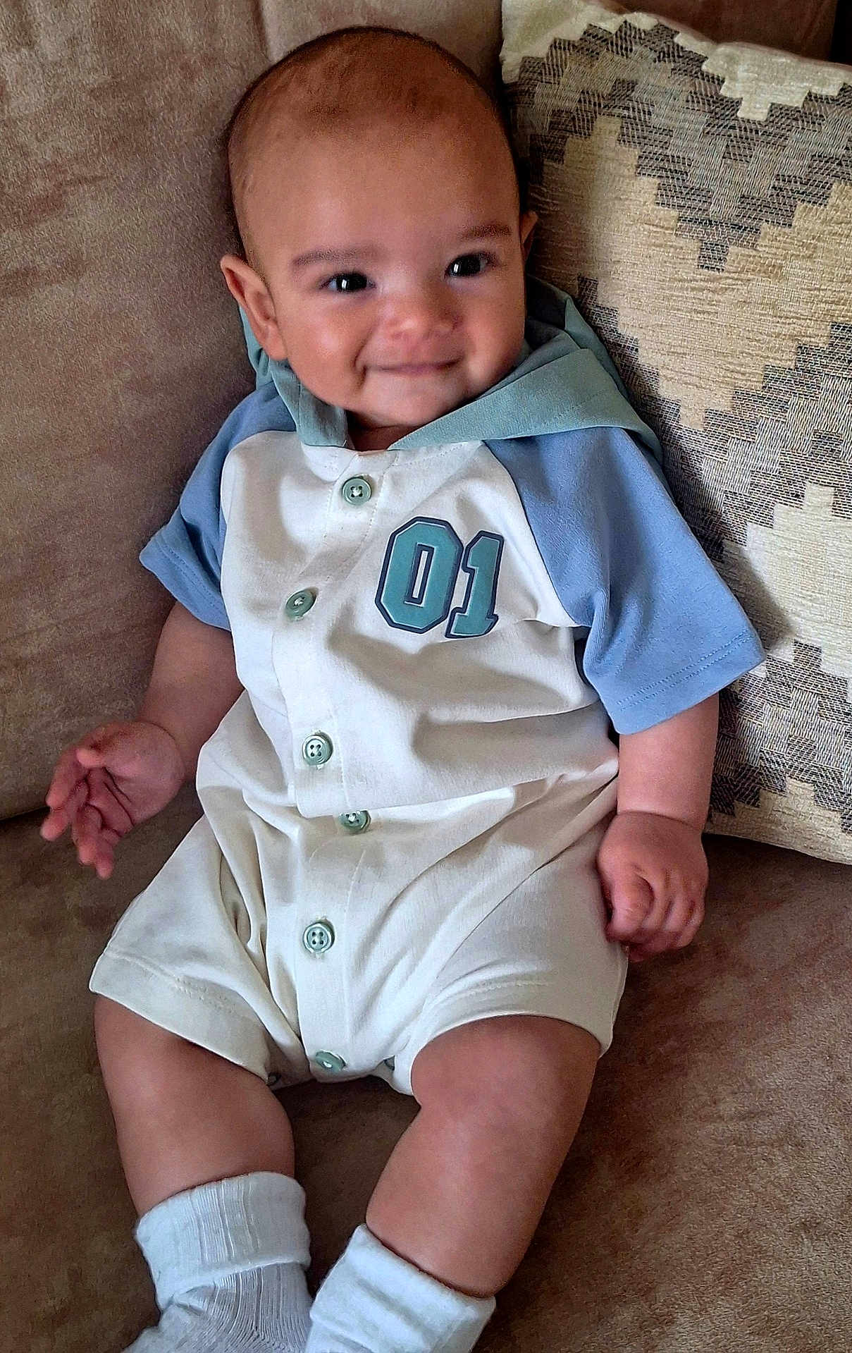 Caolán joined the competition — help win amazing prizes! baby, child, smiling, couch, pillow, onesie, clothing, infant, cute, happy, sitting, indoor, portrait, soft_furniture, patterned_pillow, person, young_child, sock, casual, relaxed