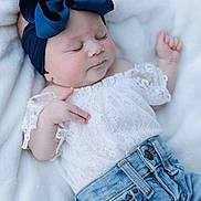 Tatum is registered to the contest to win money with this photo: baby, sleeping, blue_bow, white_lace_top, jeans, infant, soft_blanket, cute, peaceful, child, portrait, fashion, headband, closeup, relaxing, casual_clothing, adorable, resting, indoor, newborn