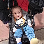 Theo is registered to the contest to win money with this photo: baby, child, smiling, stroller, clothing, bib, footwear, happy, sitting, indoor, person, infant, jacket, pants, sock, shoe, face, head, cute, seat