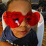 Lucas is registered to the contest to win money with this photo: child, sunglasses, heart_shaped_glasses, red_glasses, close_up, blurred, indoor, chair, dog_in_background, couch, living_room, toddler, face, playful, accessory, t_shirt, seat, wooden_floor, pet, portrait
