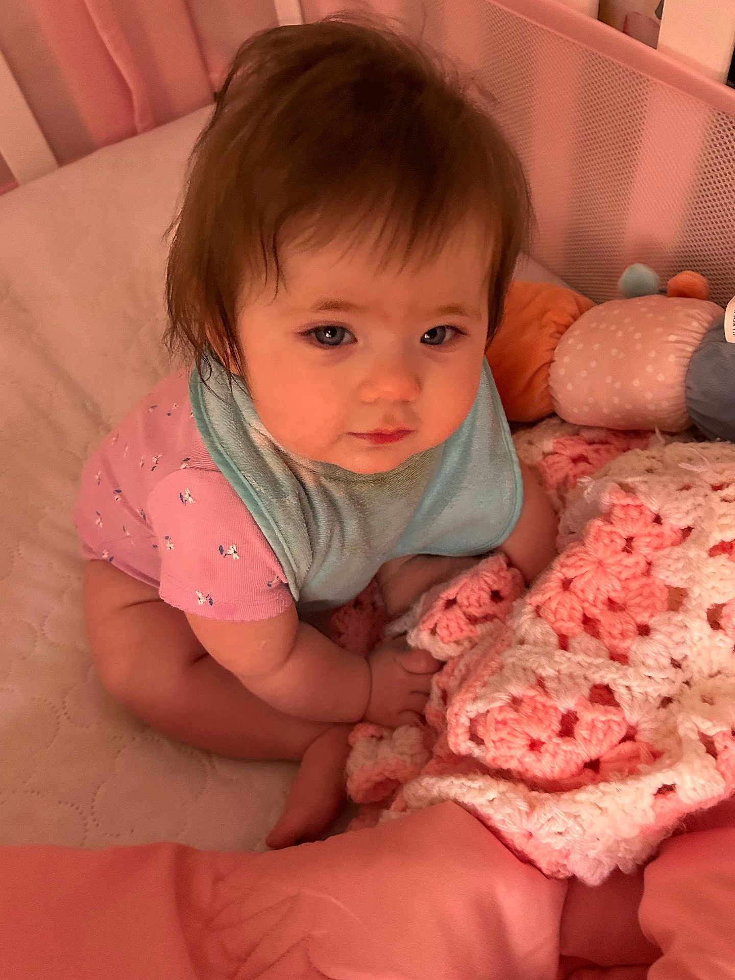 Sierra is registered to the contest to win money with this photo: baby, child, crib, blanket, plush_toy, pink, pastel_colors, clothing, sitting, infant, face, hair, eyes, cute, soft_texture, home, indoor, portrait, expression, comfort