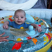 Eden participe au concours pour gagner de l'argent avec cette photo : baby, blue_clothing, child, colorful, cute, face, floatation_device, fun, hand, indoor_pool, infant, inflatable_ring, person, playful, pool, safety, smiling, swimming, toy, water