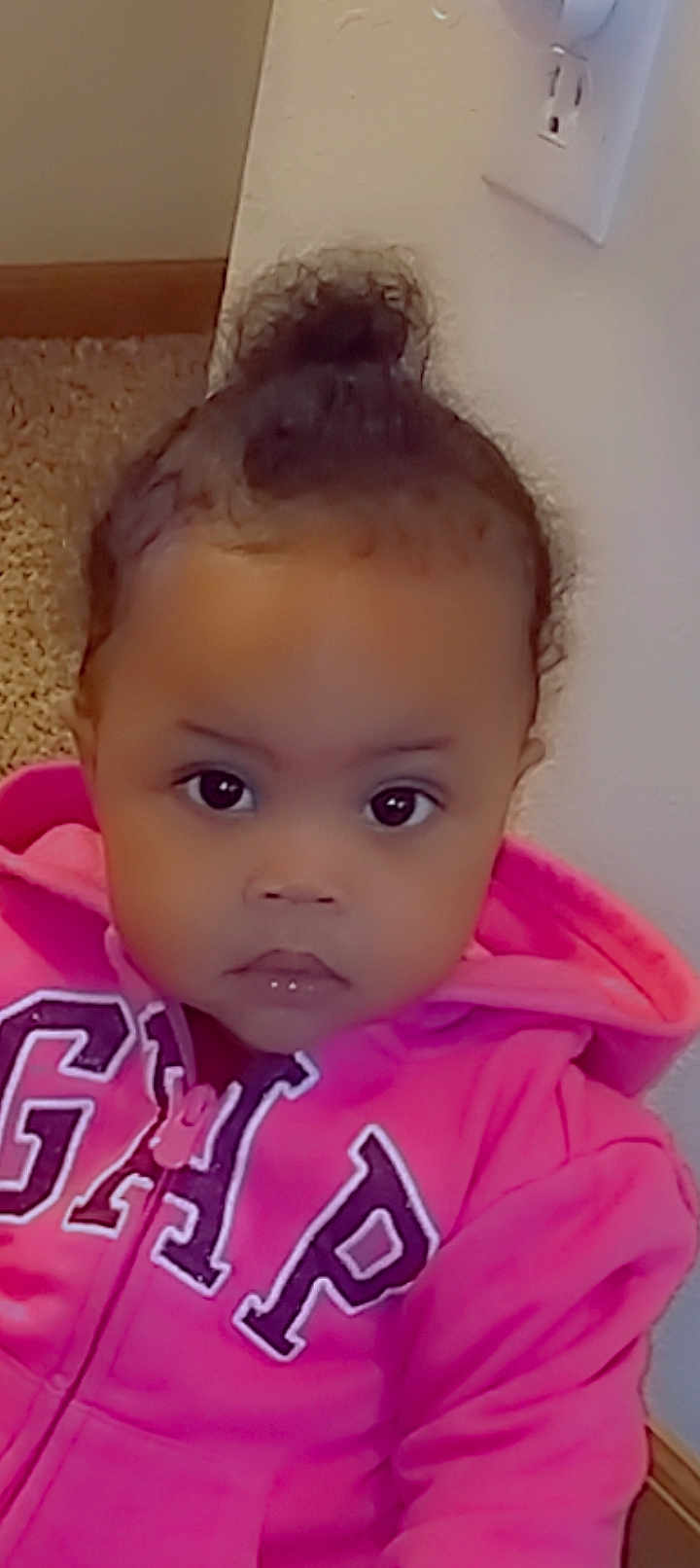 Icslyn is registered to the contest to win money with this photo: toddler, child, face, eyes, hair_bun, hoodie, pink_clothing, sitting, indoor, carpet, wall, expressionless, portrait, person, young_child, casual_clothing, baby, cute, growing_up, curious