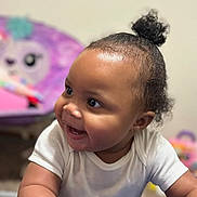Icslyn is registered to the contest to win money with this photo: baby, child, smiling, white_onesie, curly_hair, pony_tail, indoor, toys, purple_chair, cute, happy, face, person, infant, playroom, soft_focus, background_blur, cheerful, close_up, skin