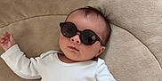 Louis a rejoint le concours — aidez-le/la à gagner de superbes lots ! baby, baby_clothes, child, cool, cute, face, fashion, hand, head, indoor, infant, laying_down, person, portrait, relaxing, soft_cushion, stylish, sunglasses, text_on_clothing, white_onesie