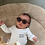 baby, baby_clothes, child, cool, cute, face, fashion, hand, head, indoor, infant, laying_down, person, portrait, relaxing, soft_cushion, stylish, sunglasses, text_on_clothing, white_onesie