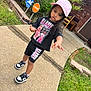 child, kid, barbie, pink_cap, black_outfit, shorts, tshirt, sneakers, nike, sidewalk, grass, brick_house, outdoor, curious, person, walking, street_sign, greenery, fashion, casual