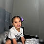 Loreanny Kataleya joined the competition — help win amazing prizes! child, girl, smile, bed, braids, purple_bow, white_shirt, black_shorts, indoor, wall, happy, person, cute, youth, portrait, bedroom, furniture, fabric, home, sitting