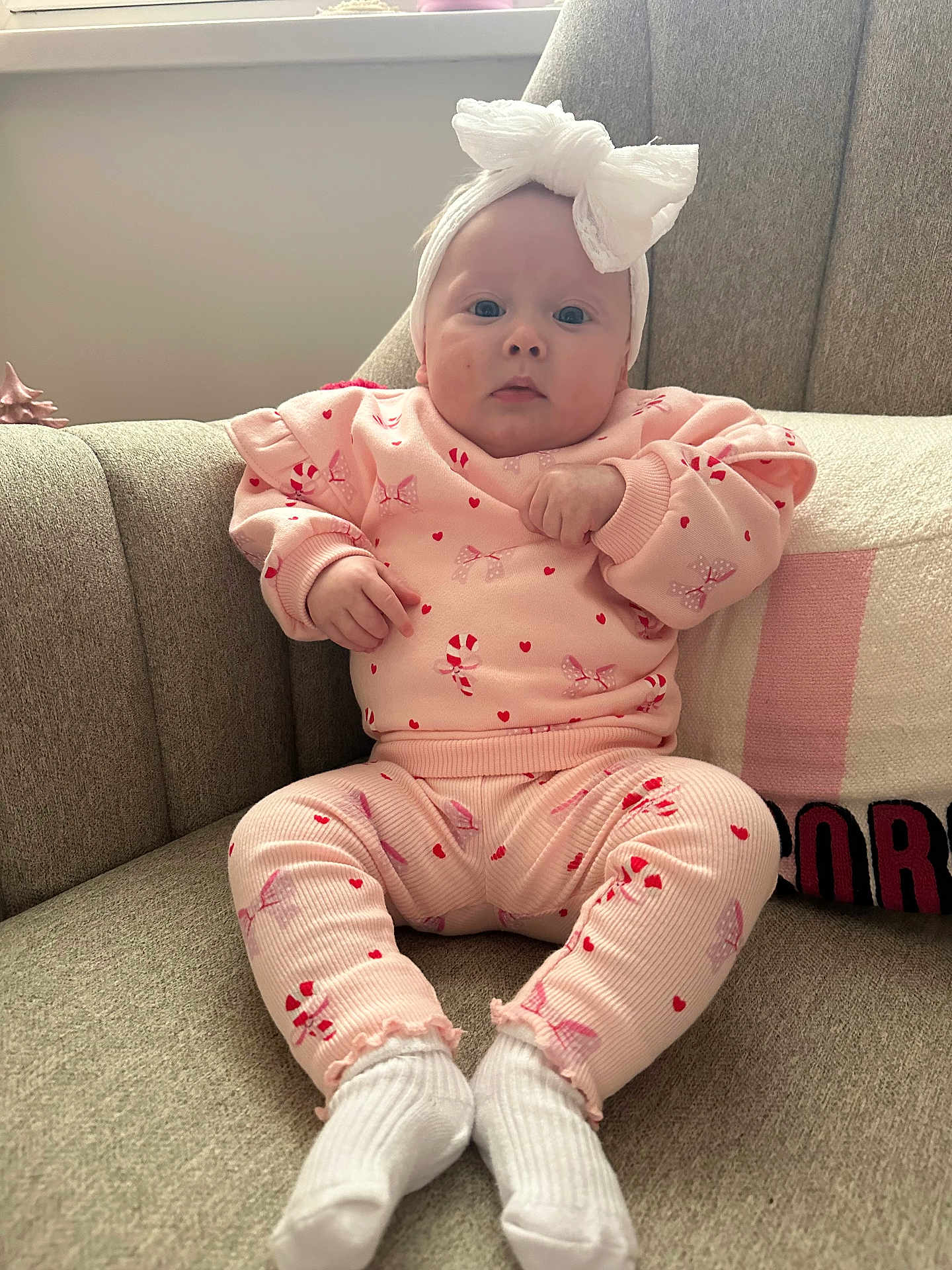 Marnie joined the competition — help win amazing prizes! baby, infant, pink_clothing, headband, bow, candy_cane_pattern, socks, couch, furniture, indoor, portrait, child, seated, cute, soft_light, cozy, face, hands, window_light, relaxed