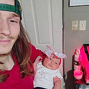 Madilyn joined the competition — help win amazing prizes! man, baby, infant, cap, long_hair, smile, indoor, door, calendar, bottle, table, light, pink_bow, clothing, tattoo, hand, face, person, holding, casual