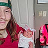 man, baby, infant, cap, long_hair, smile, indoor, door, calendar, bottle, table, light, pink_bow, clothing, tattoo, hand, face, person, holding, casual