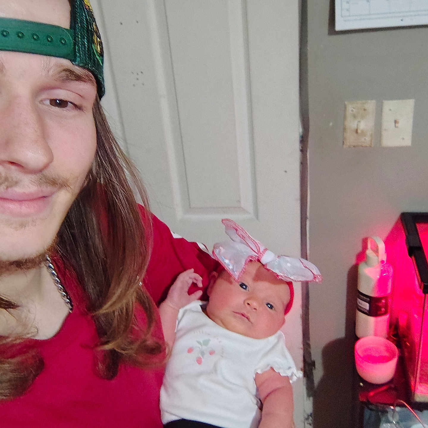 Madilyn joined the competition — help win amazing prizes! man, baby, infant, cap, long_hair, smile, indoor, door, calendar, bottle, table, light, pink_bow, clothing, tattoo, hand, face, person, holding, casual
