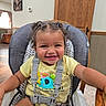 toddler, child, high_chair, smiling, happy, baby, indoors, wood, hair, pigtails, clothing, seatbelt, furniture, face, person, room, window, curtain, table, shirt