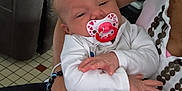 Nëylia a rejoint le concours — aidez-le/la à gagner de superbes lots ! baby, pacifier, adult_hand, toy, indoor, couch, arm, person, clothing, bracelet, floor, television, furniture, plush_toy, beads, white_clothing, holding, closeup, home, relaxing