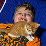 child, kitten, cat, ginger_cat, white_paws, smiling, portrait, bed, bedroom, blue_blanket, orange_shirt, casual_clothing, indoors, pet, cuddling, sitting, lying_down, whiskers, furry, happy
