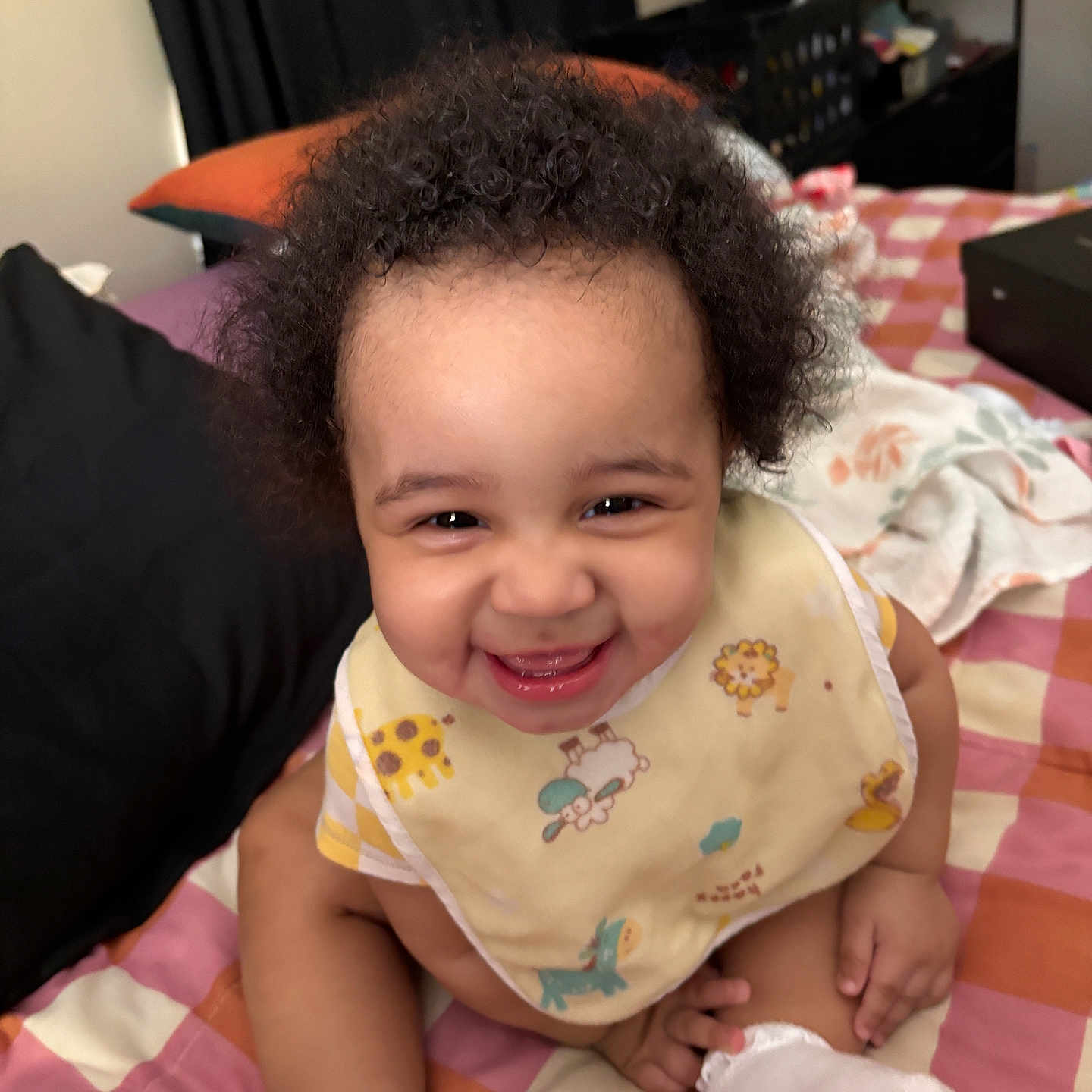 Enilyah joined the competition — help win amazing prizes! baby, child, smiling, curly_hair, bib, socks, bed, pillow, blanket, indoor, person, happy, cute, room, furniture, sitting, infant, young_child, face, portrait
