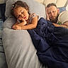 child, man, sleeping, bed, blanket, pillow, indoor, rest, hair_clips, curly_hair, beard, casual_clothing, relaxation, cozy, family, nap, comfort, tired, peaceful, portrait