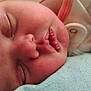 baby, sleeping, close_up, face, rosy_cheeks, infant, soft_texture, clothing, button, peaceful, resting, skin, head, eyelashes, mouth, nose, newborn, portrait, indoors, quiet