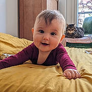 Augustine participe au concours pour gagner de l'argent avec cette photo : baby, infant, smiling, bed, blanket, cat, chair, window, indoor, furniture, curtain, person, cute, drool, maroon_clothing, tabby_cat, green_chair, yellow_bedspread, relaxed, daylight