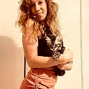 Minoush participe au concours pour gagner de l'argent avec cette photo : woman, cat, kitten, smiling, curly_hair, holding, indoor, portrait, casual_clothing, skirt, black_top, light_background, feline, pet, happy, cute, young_adult, warm_lighting, friendly, cozy