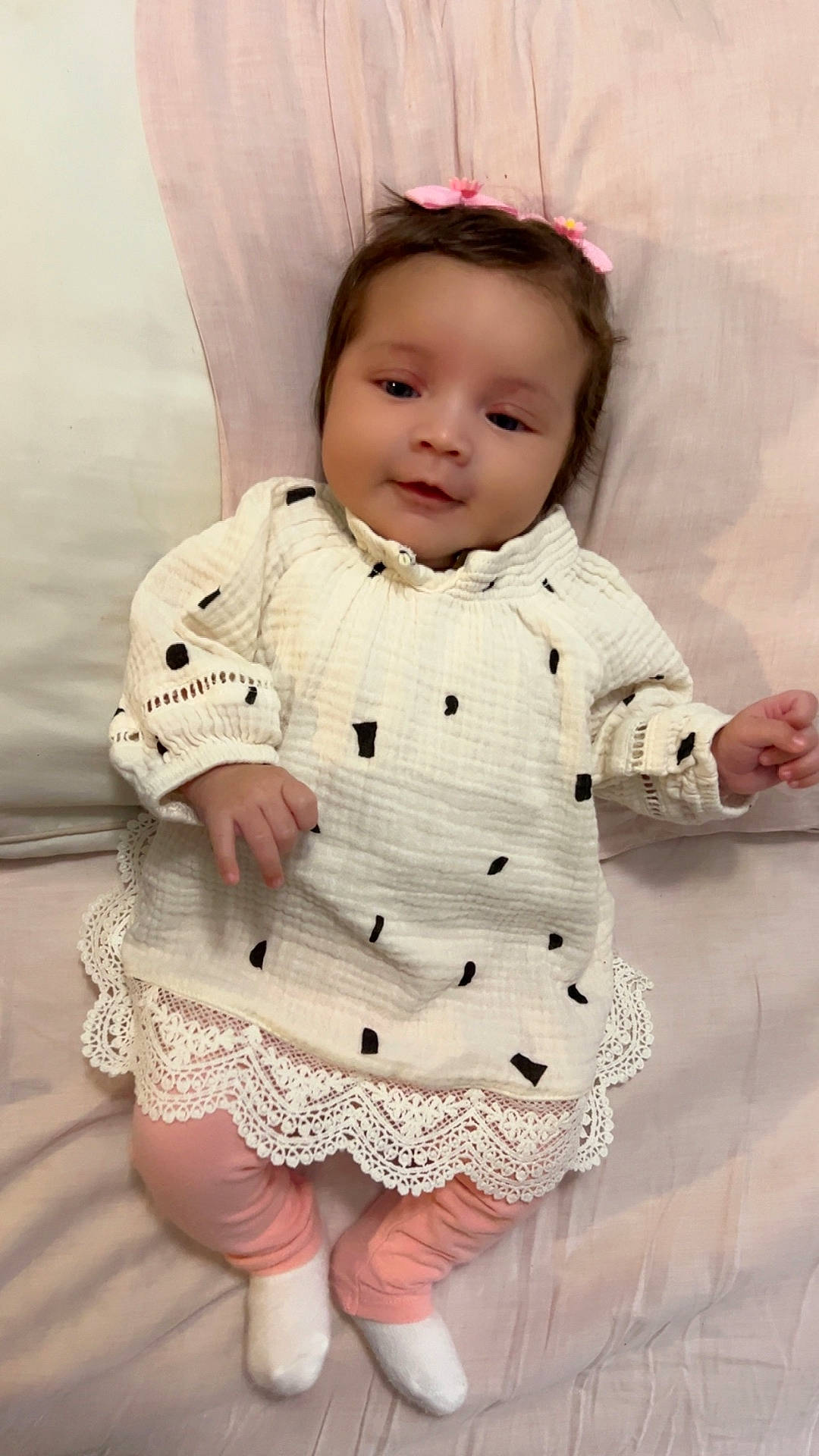 adorable, baby, black_spots, blanket, child, cozy, cute, face, hair_clips, indoors, infant, lace_trim, lying_down, person, pink_leggings, portrait, smiling, soft_fabric, white_dress, white_socks
