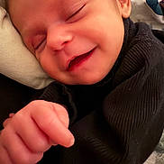 Sabrina is registered to the contest to win money with this photo: baby, infant, sleeping, smile, hand, face, black_clothing, cozy, closeup, peaceful, newborn, skin, cute, child, portrait, soft, resting, young, human, indoors